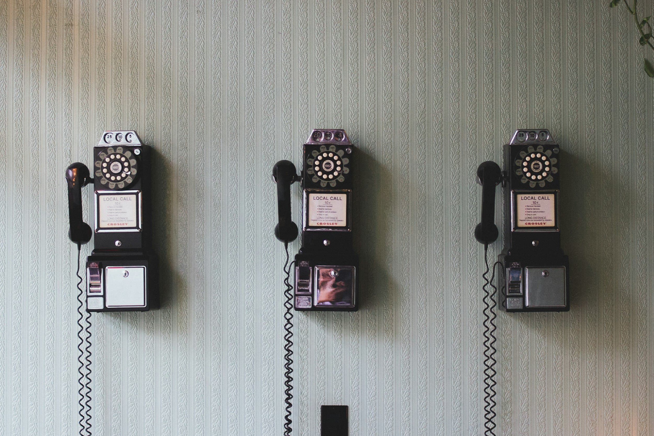 Tre gamle veggtelefoner på rad på en vegg